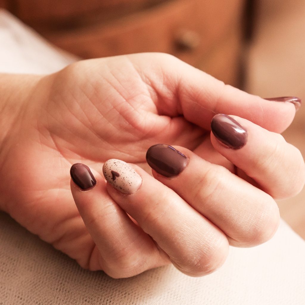 Manicure con smalto semipermanente color cioccolato, sull'anulare una nail art minimal con base panna e cuoricino cioccolato, top con brillantini, trattamento professionale per unghie curate e resistenti