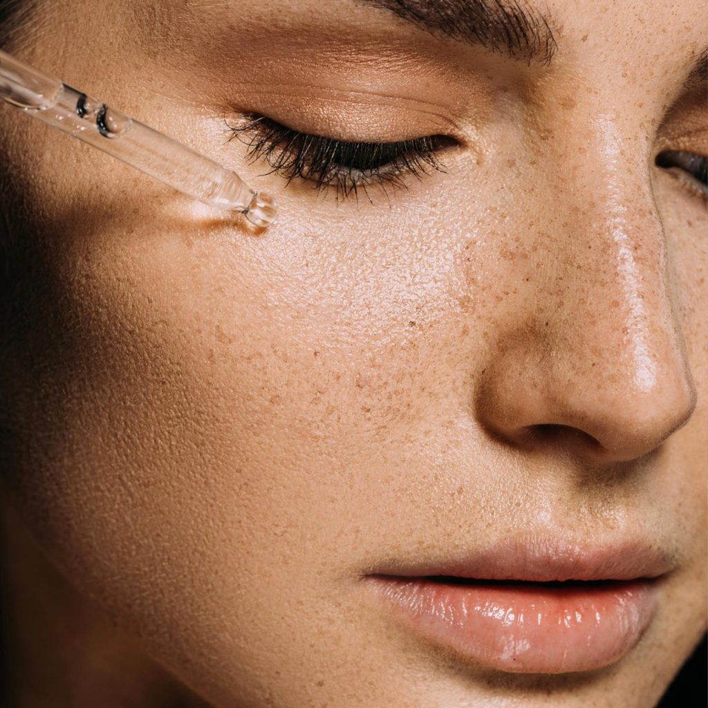 Applicazione di siero antiossidante su pelle del viso con pipetta, trattamento skincare per proteggere e illuminare la pelle