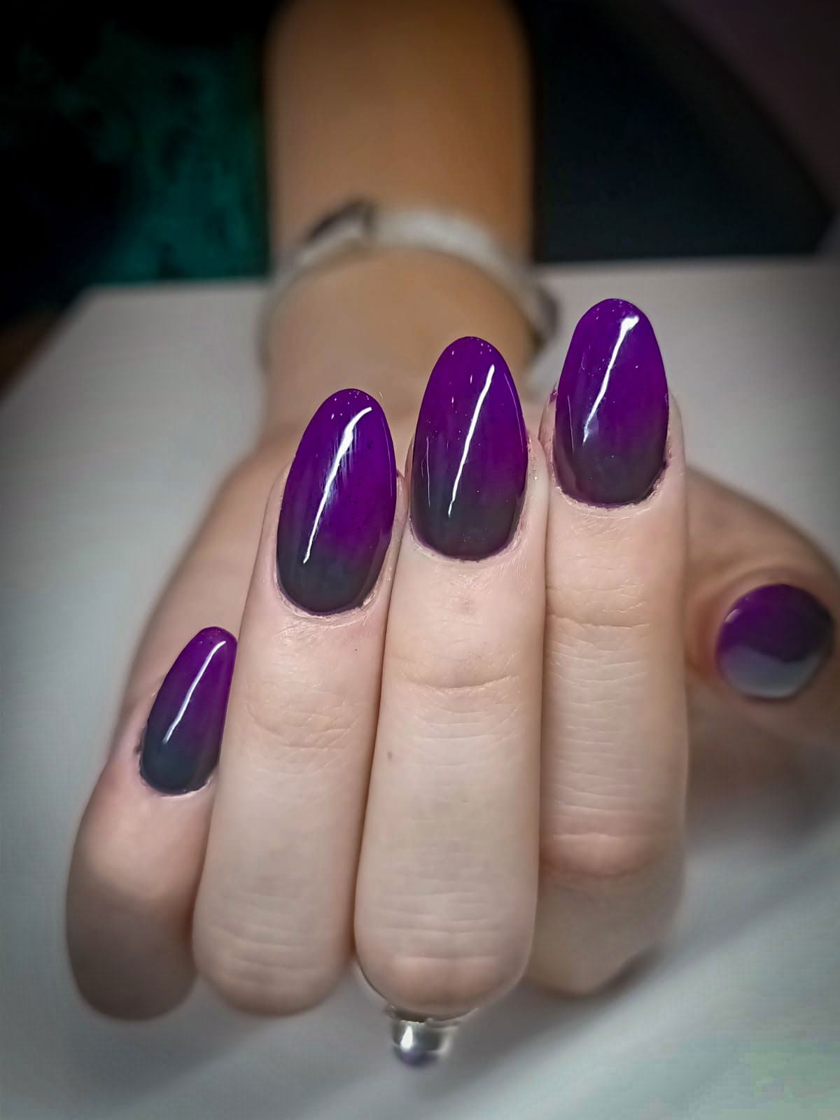 Manicure con gel su unghie dalla forma ovale, smalto sfumato nei toni viola e nero con effetto lucido professionale